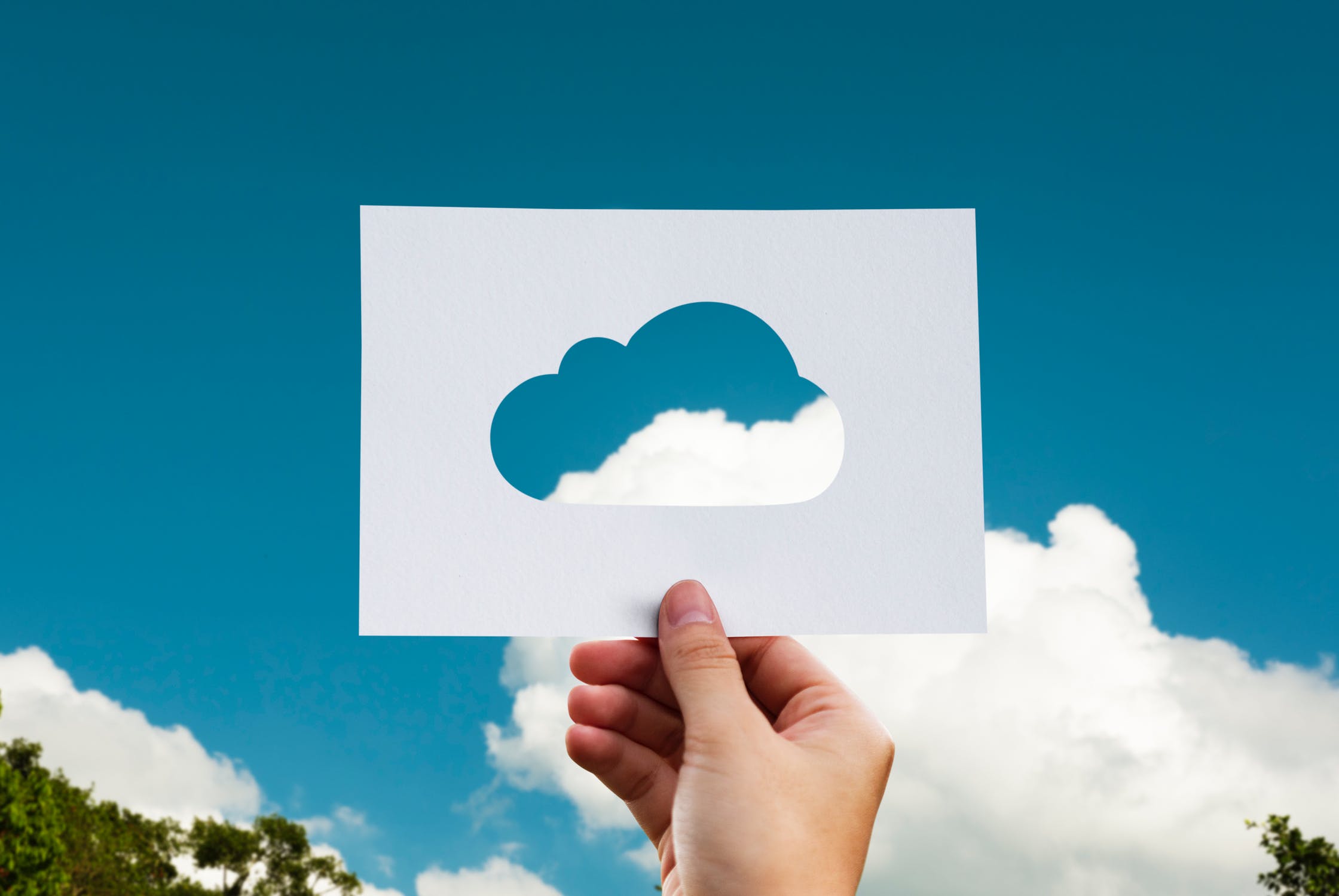 Person holding a piece of paper up to sky with cloud cut out