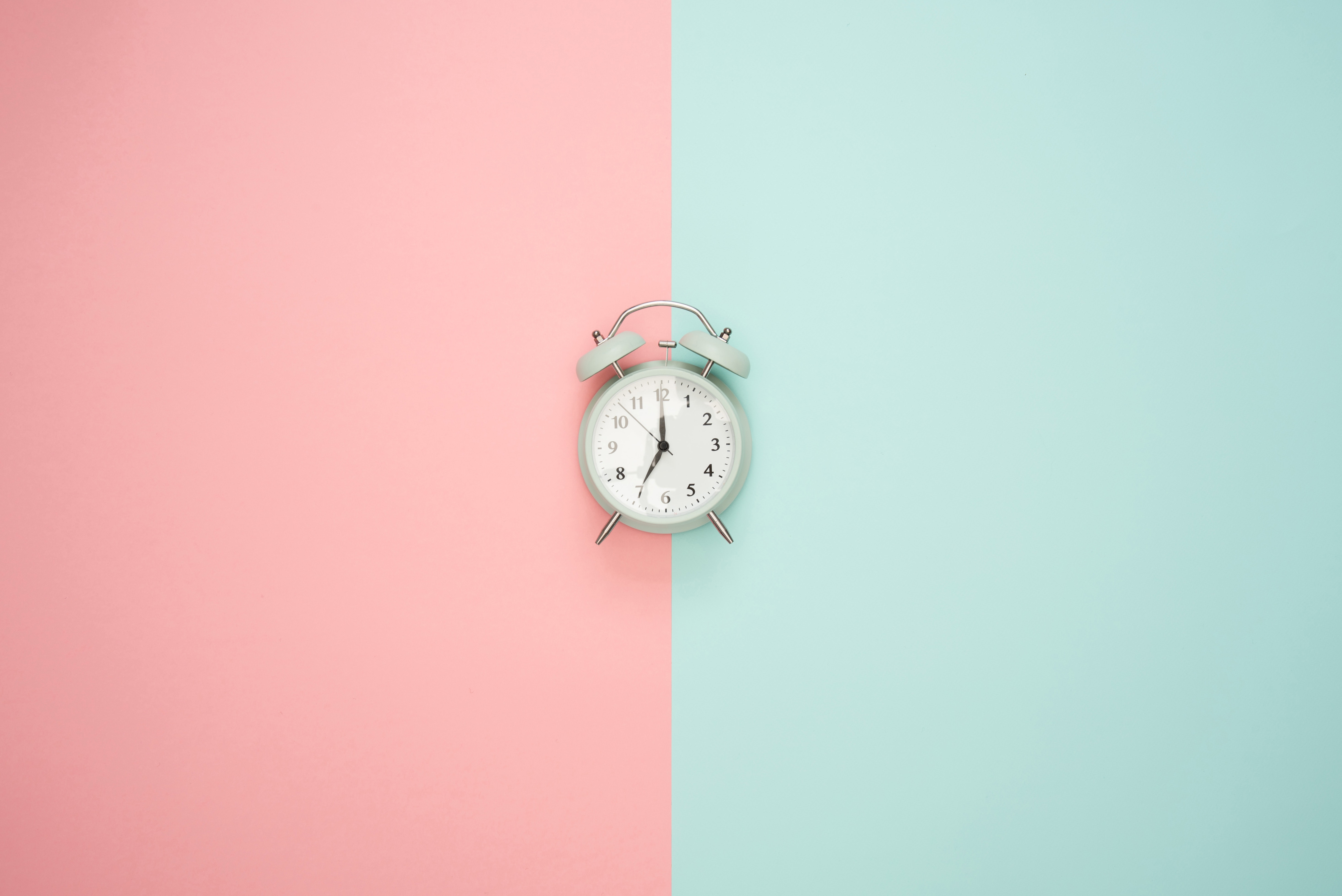 Old fashioned alarm clock against a pink and teal background